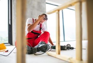 A construction worker sits on the floor and holds his head in pain