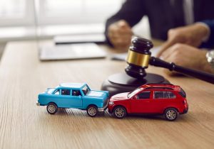 A blue and red toy car crashing into each other in front of a wooden gavel.