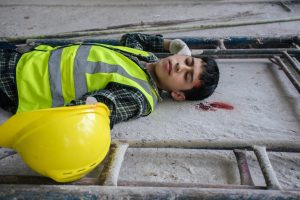 A construction worker lying on the ground suffering a head injury.