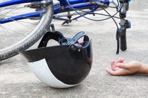A black and white bicycle helment and blue bike with a strewn hand on the road.