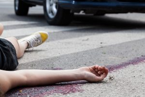 A pedestrian laying in a pool of blood on the road. The wheels of a car can be seen in the background