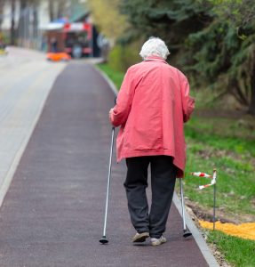 An elderly person using mobility aids on the pavement. 