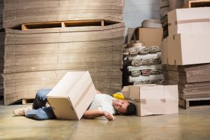 A man lying on the floor with a box on top of him after a workplace injury. 